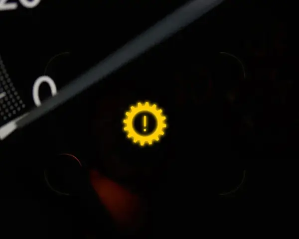 Gelbes Warnlicht mit einem Zahnrad und Ausrufezeichen im Auto-Armaturenbrett. Ein Zeichen für ein Problem mit dem Getriebe.