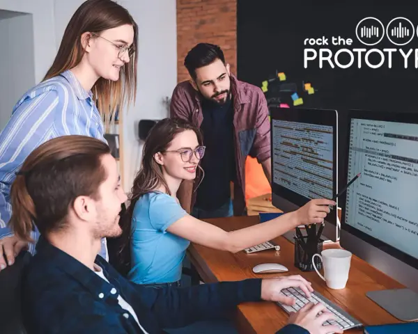 Ein Team von vier Personen arbeitet im **mob programming** an einem Projekt. Sie blicken auf zwei Bildschirme mit Code.