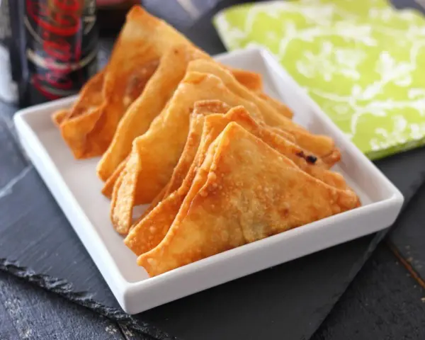 Wontons fritos dorados y crujientes en un plato blanco.