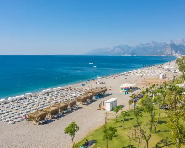 Piękna plaża z rzędami leżaków i parasoli, gdzie jest Antalya. Błękitne morze i góry w tle tworzą idealny krajobraz.
