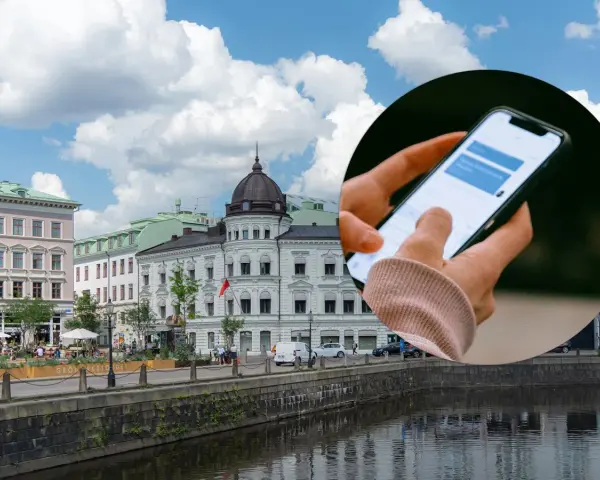 Dłoń trzymająca smartfon z widocznym oknem czatu na tle miejskiego krajobrazu z budynkami i rzeką.