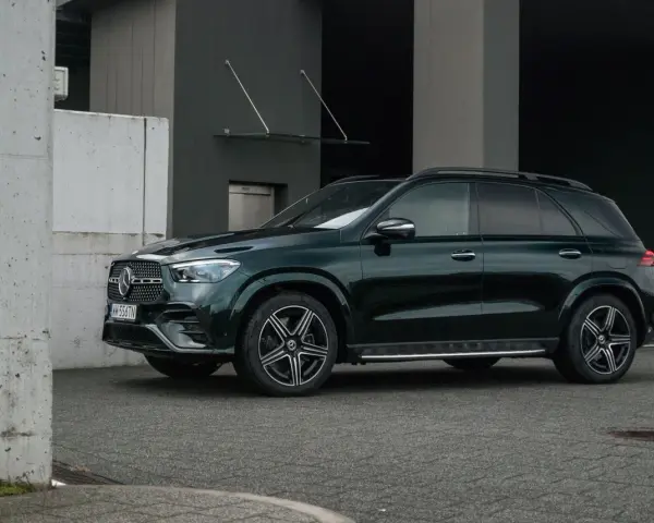 Elegancki, ciemnozielony Mercedes GLE 2025 zaparkowany przed nowoczesnym budynkiem.