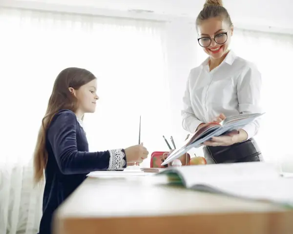 Nauczycielka pomaga dziecku z dysleksją w szkole, cierpliwie tłumacząc materiał z książki.