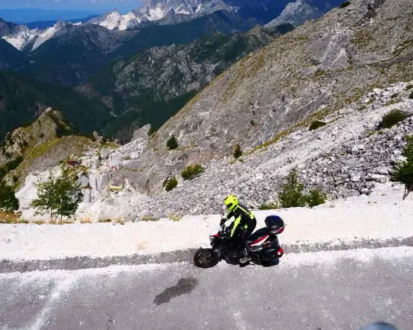 Motociclista in abbigliamento giallo fluo affronta il passo del vestito, tra cave di marmo e montagne imponenti.