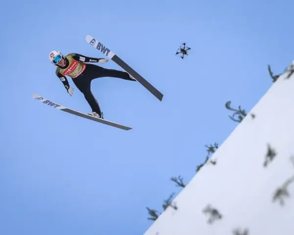 Skoczek narciarski w locie, z dronem w tle. Zastanawiasz się, ile waży skoczek narciarski, by osiągnąć taką odległość?