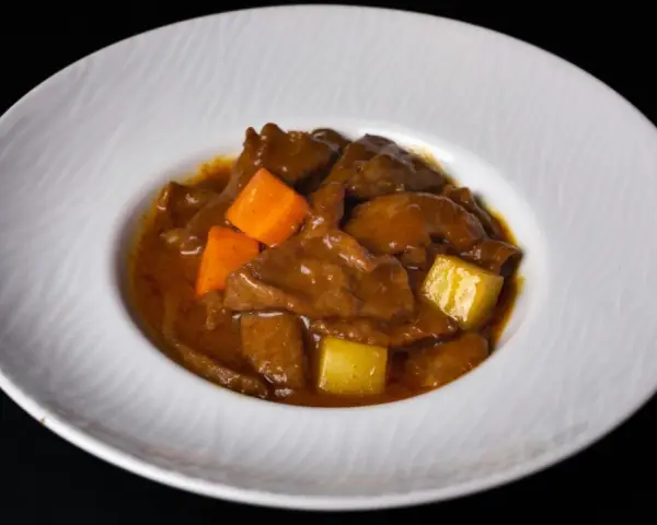 Un delicioso estofado de ternera con trozos de zanahoria y patata en una salsa espesa y aromática, servido en un plato blanco.