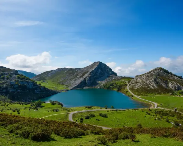 Lago azul rodeado de montañas verdes y caminos sinuosos, parte de la red de parques nacionales.