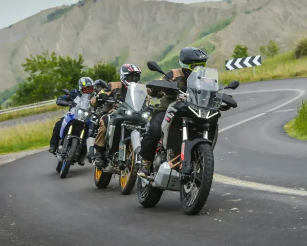 Quattro motociclisti in fila su una strada tortuosa tra colline verdi. Sei motociclista se ami l'avventura.