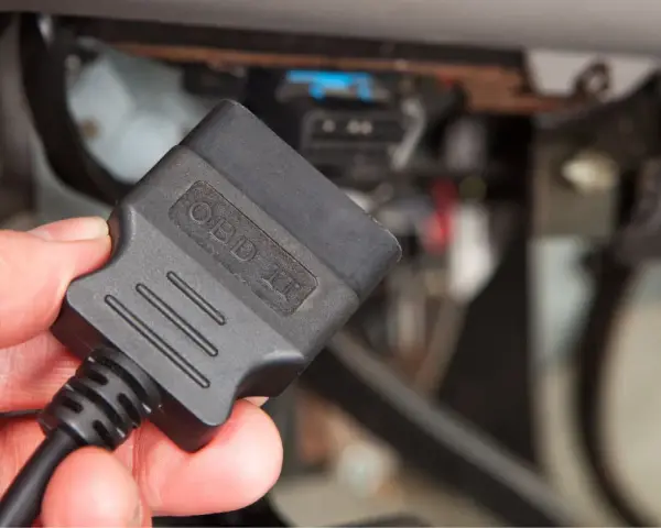 Dłoń trzyma adapter OBD II, gotowy do podłączenia i sprawdzenia kodu błędu w samochodzie.