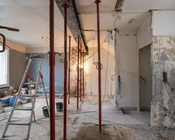 Chantier en cours : étais rouges soutenant un linteau, murs abattus, échelle et matériaux. Préparation pour une ouverture mur porteur.