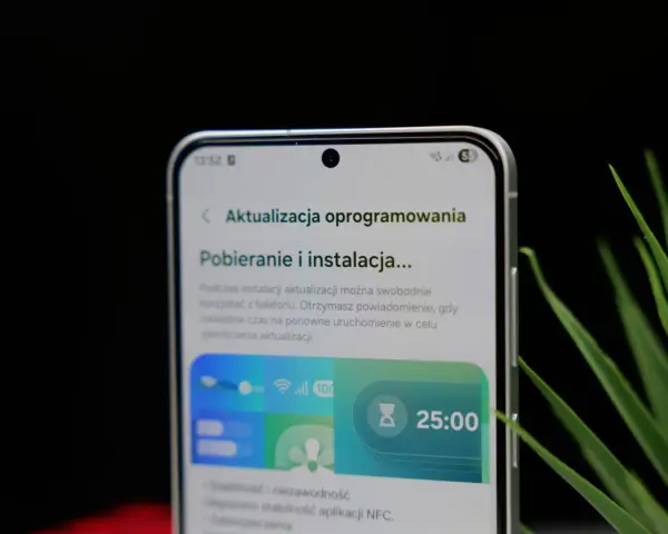 Telefon z interfejsem One UI 8.5 pokazuje ekran pobierania aktualizacji oprogramowania. Widoczny jest zegar 25:00.