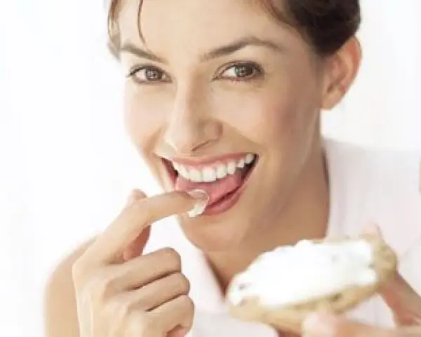 Une femme savoure une bouchée de pain avec de la saint agur crème enceinte, un sourire aux lèvres.