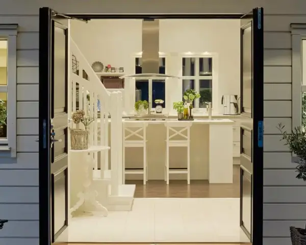 Välkomnande entré inspiration utomhus. Öppna dörrar leder in till ett ljust kök med köksö och trappa.
