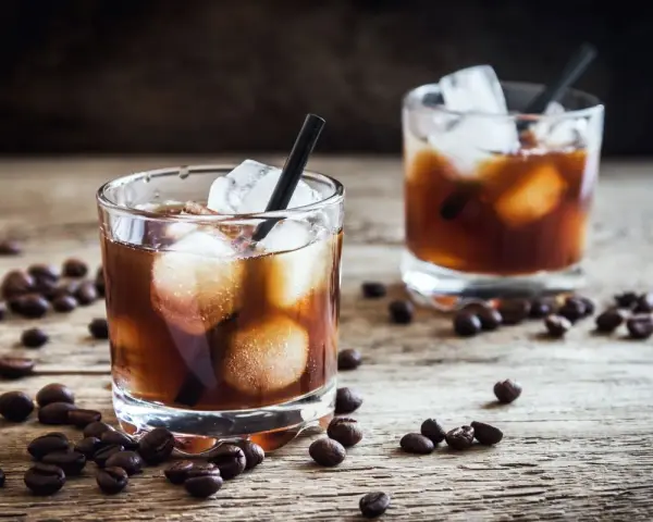 Dwa szklanki z lodem i ciemnym napojem, otoczone ziarnami kawy. Idealny czarny rusek drink na drewnianym blacie.
