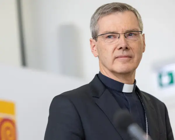 Ein Bischof mit Brille und Soutane spricht in ein Mikrofon. Die Frage "wer bezahlt den Bischof" wird hier nicht beantwortet, aber das Bild zeigt ihn bei einer öffentlichen Rede.