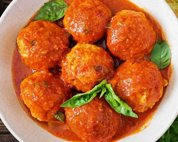 Polpette di pane succulente in salsa di pomodoro, guarnite con foglie di basilico fresco. Un piatto che sa di casa.