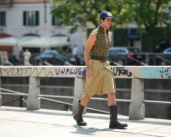 Uomo con un elegante outfit sportivo estivo: gilet a fantasia, bermuda color sabbia e stivali.