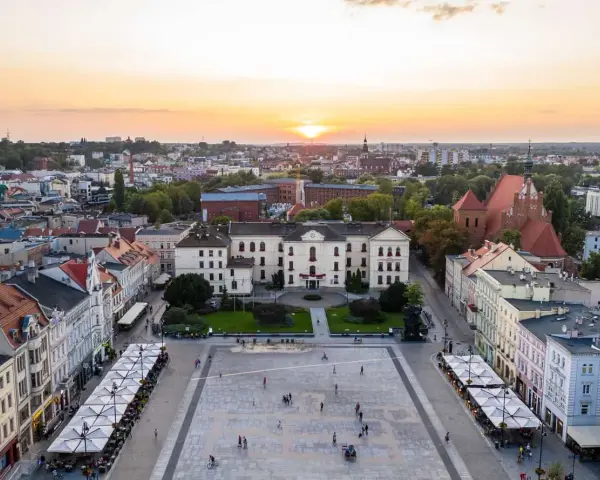 Zachód słońca nad rynkiem, gdzie widać piękną pierzeję kamienic i ratusz. Ludzie spacerują po placu, ciesząc się ciepłym wieczorem.