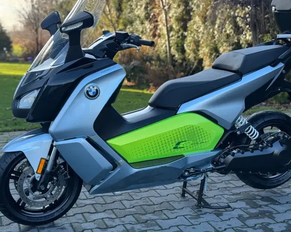Srebrno-czarny skuter elektryczny BMW C Evolution z zielonym akcentem i napisem "C Evolution" na boku, stojący na chodniku.