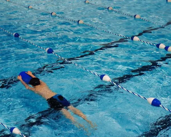 Un nageur utilise une planche bleue dans une piscine avec des lignes de bouées bleues et blanches.