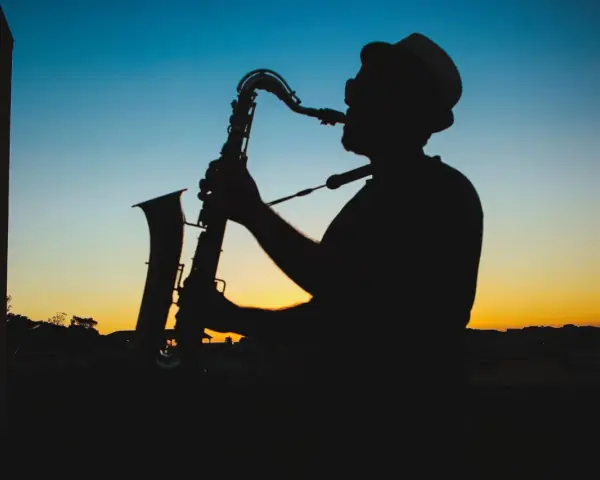 Sylwetka muzyka w kapeluszu grającego na saksofonie o zachodzie słońca. Prawdziwy mistrz, jeden z najlepszych bluesmanów świata.