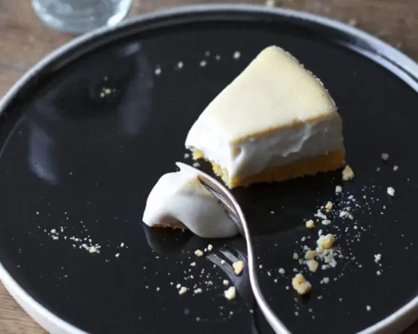 Un trozo de tarta de queso cremoso, con una porción ya probada, sobre un plato negro.