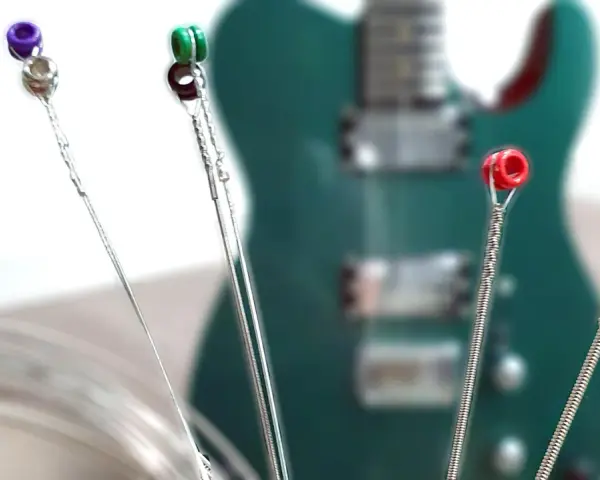 Vier Gitarrensaiten mit farbigen Enden (lila, grün, rot, gold) liegen vor einer grünen E-Gitarre. Die besten E-Gitarren-Saiten für deinen Sound.