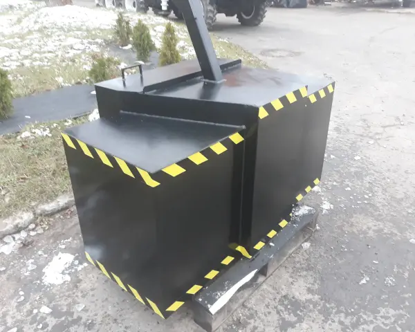 Czarny, metalowy balast do ciągnika z żółto-czarnymi pasami ostrzegawczymi, stojący na drewnianej palecie.