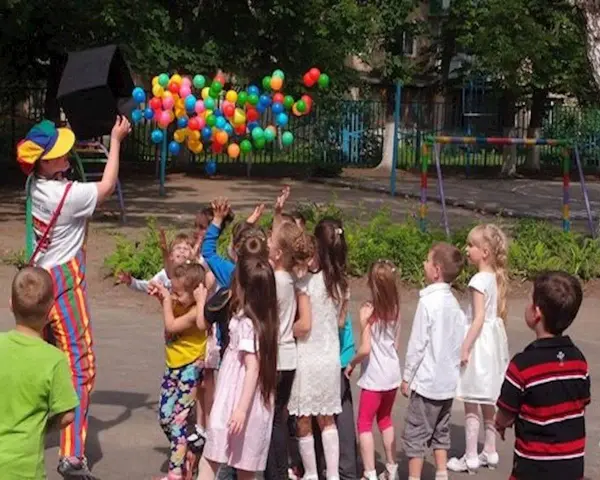 Klaun wypuszcza balony dla dzieci. Czy są zerówki w szkołach? Dzieci cieszą się zabawą na świeżym powietrzu.