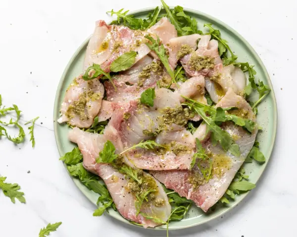 Deliziosi antipasti di pesce crudo, affettati sottili e conditi con erbe aromatiche e olio, serviti su un letto di rucola fresca.