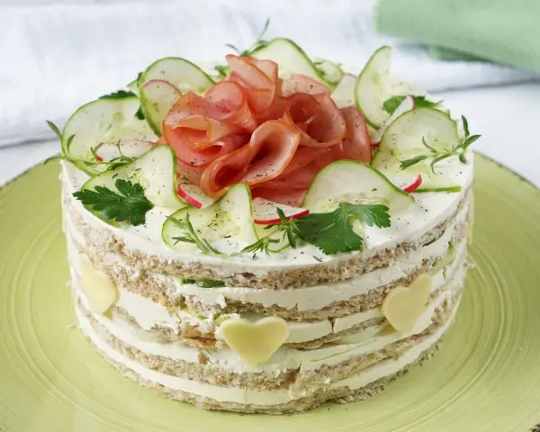Herzhafter Kuchen mit Schichten aus Brot, Frischkäse, Gurken und Schinken. Dekoriert mit Radieschen, Kräutern und Käseherzen.