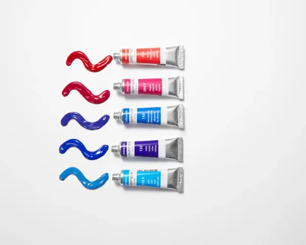 Des tubes de gouache ou acrylique Caran d'Ache libèrent des traînées de couleurs vives : rouge, magenta, bleu outremer, violet et cyan.