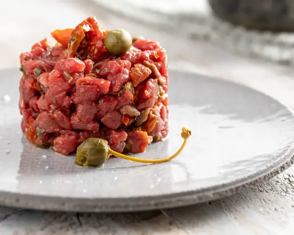 Deliziosa tartare di manzo, guarnita con capperi e pomodori secchi, servita su un piatto grigio.