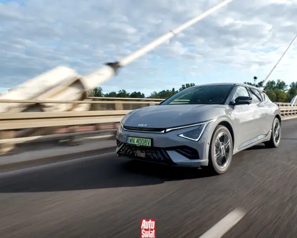 Szary Kia EV6 jedzie po moście w słoneczny dzień.