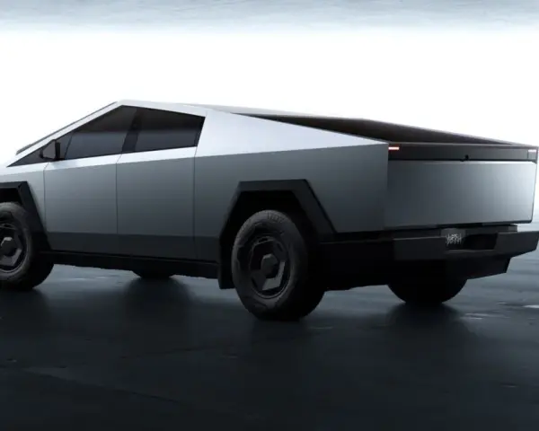 Futurystyczny Tesla Cybertruck w kolorze srebrnym, z ostrymi krawędziami i masywnymi kołami, prezentuje się na ciemnej, betonowej podłodze.