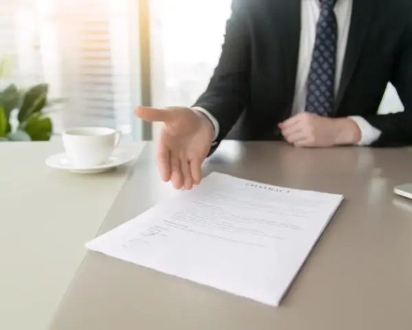 Biznesmen wyciąga rękę do uścisku nad dokumentem, symbolizującym rezygnację z pracy.