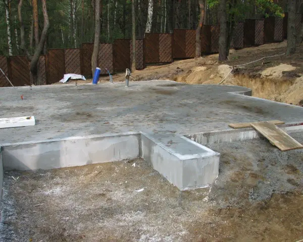 Fundament płytowy w trakcie budowy, z widocznymi elementami betonowymi i zbrojeniem.