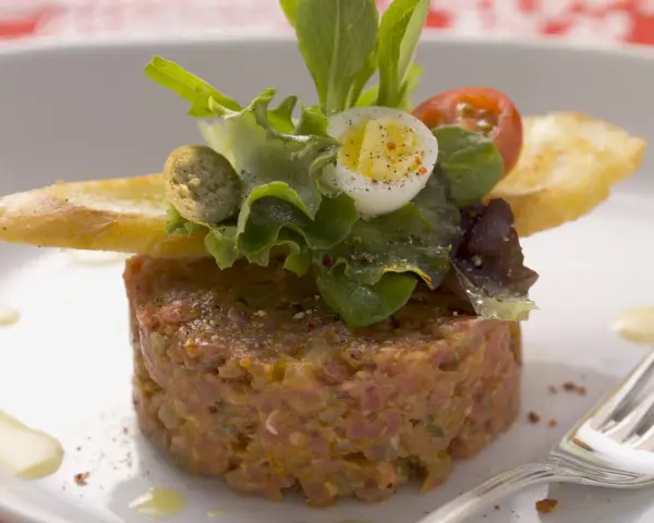 Un délicieux tartare de bœuf, garni d'une salade fraîche, d'un œuf de caille et de croûtons. Une recette parfaite pour un repas raffiné.
