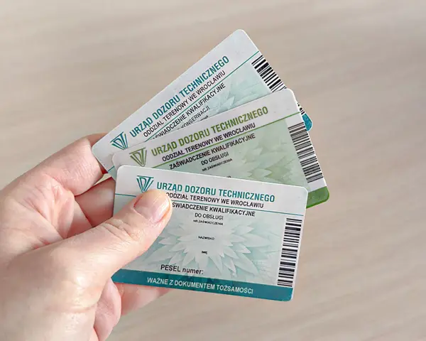 Dłoń trzyma kilka zaświadczeń kwalifikacyjnych Urzędu Dozoru Technicznego, potwierdzających uprawnienia HDS.