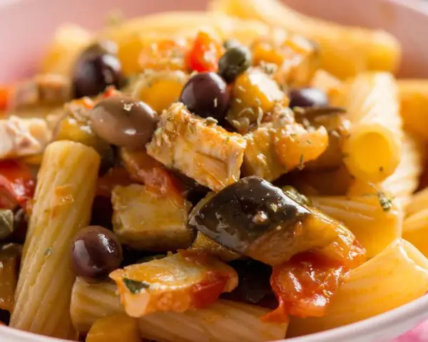 Un piatto invitante di pasta con pesce, arricchito da olive nere, capperi e verdure colorate.