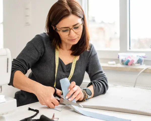 Une couturière utilise des ciseaux pour couper du tissu, montrant l'importance des différents types de ciseaux de couture pour un travail précis.