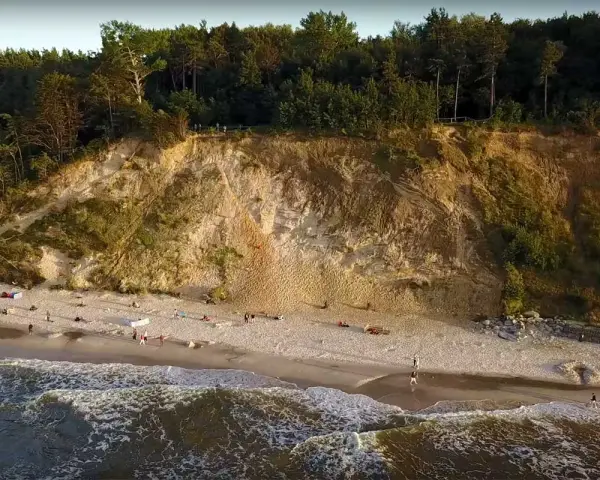 Plaża u stóp najwyższego klifu w Polsce. Ludzie spacerują po piasku, fale obmywają brzeg.