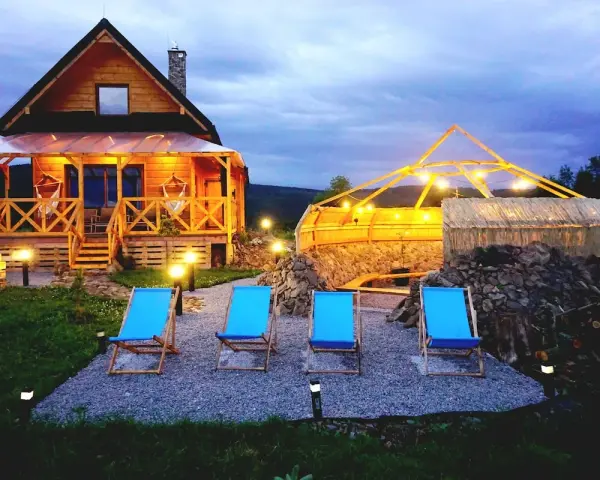 Drewniany domek z werandą, jacuzzi pod zadaszeniem i leżakami w malowniczej okolicy.