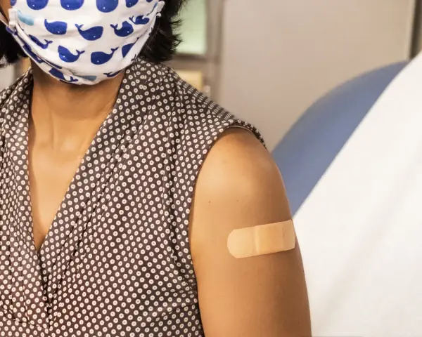 Osoba w maseczce z wielorybami ma plaster na ramieniu po szczepieniu. Dbanie o zdrowie, w tym szczepionka HPV, to ważny krok.