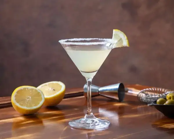 Elegancki drink Martini Bianco z cytrynową ozdobą i słonym rantem, obok połówki cytryny i oliwek.