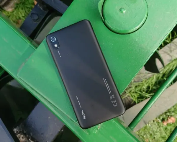 Czarny telefon Xiaomi Redmi 7 leży na zielonej, metalowej ławce.