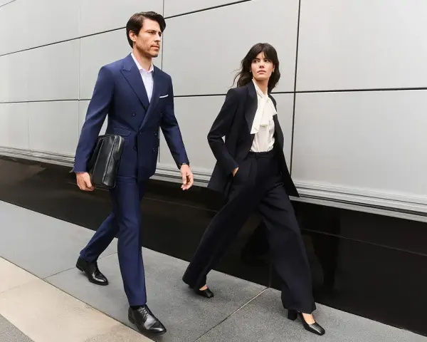 Para idąca w eleganckim business attire, mężczyzna w granatowym garniturze, kobieta w czarnym.