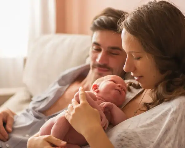 Mama tuli noworodka, tata patrzy z miłością. To piękny obraz opieki na żone po porodzie, pełen czułości i wsparcia.