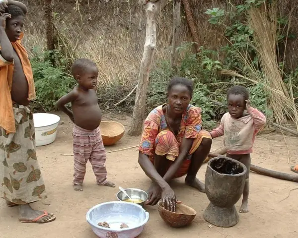 Dzieci i matka w tradycyjnej chacie w Burkina Faso. Kobieta przygotowuje posiłek, a dzieci obserwują.