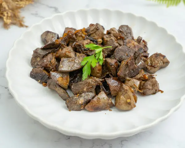 Plato de asadura de cordero salteada, con trozos oscuros y jugosos, adornado con una ramita de perejil fresco.